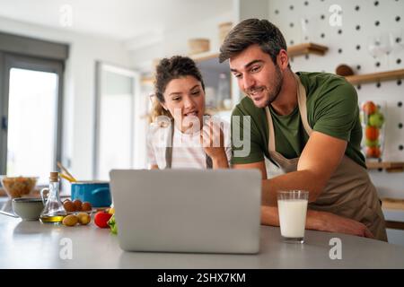 Young couple using laptop computer to take part in online culinary workshop, cooking together Stock Photo