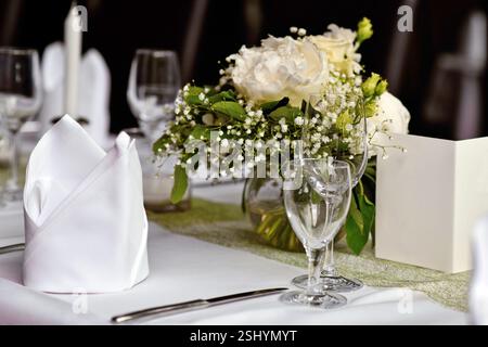 Beautiful white flower bouquets with drinking glasses and cloth napkin at Wedding table setting Stock Photo