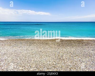 Clean pebble beach and the turquoise blue water of the calm sea on a sunny day. Travel and tourism landscape background, copy space. Stock Photo