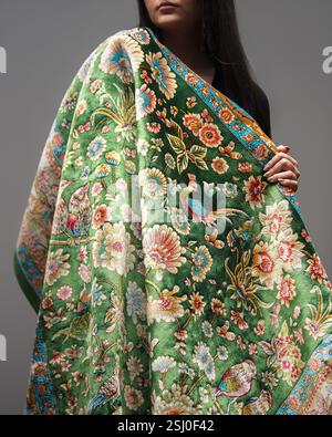 Green floral and bird patterned rug displayed by a woman, showcasing its vibrant colors and detailed design Stock Photo