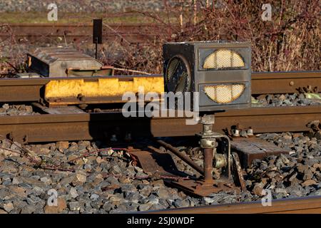 A railway signal control stands prominently beside the tracks, catching the sunlight. Surrounding gravel and track adjustments highlight the importanc Stock Photo