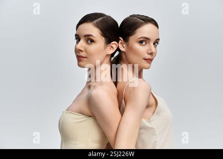 Two pretty twin sisters stand back to back, displaying their striking beauty and connection. Stock Photo