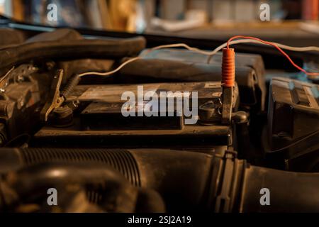 Close-Up of a Car Battery with Red Clamp and Wiring in an Automotive Workshop. Stock Photo