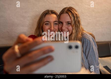 Two cheerful women taking a selfie with a smartphone while relaxing on a couch Stock Photo