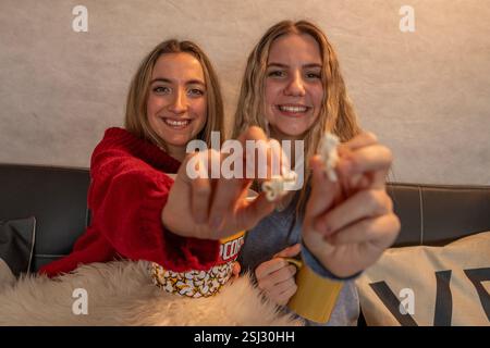 Two cheerful female friends enjoying a movie night, sharing popcorn and having fun together on a comfortable couch Stock Photo