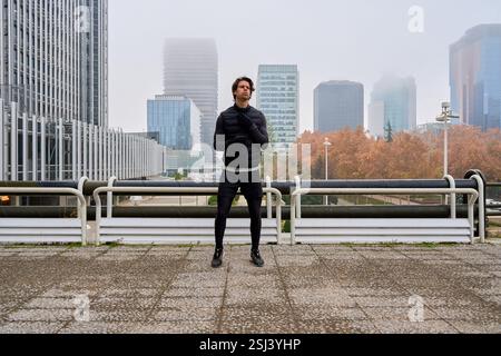 Male athlete preparing for a run in a foggy urban setting, embracing the chill of winter while focusing on fitness and determination Stock Photo
