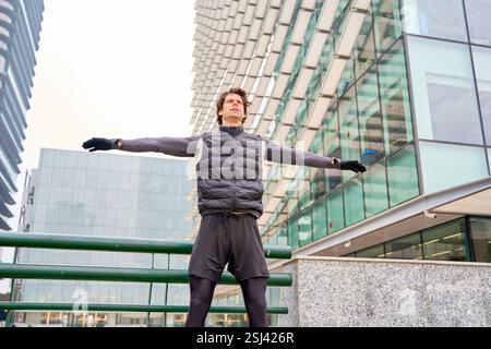 Male athlete performing warm-up exercises in a modern city setting, promoting healthy urban living Stock Photo