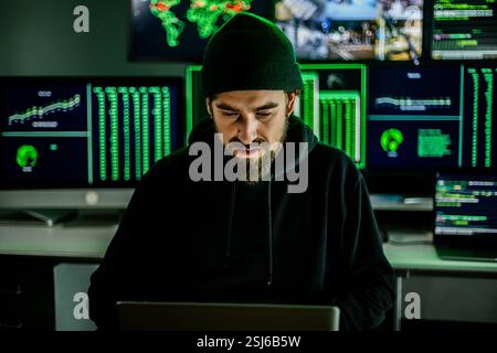 Young hacker man breaking into corporate servers from his home office Stock Photo