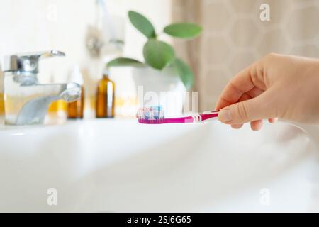 Brushing teeth before bed, woman holds a toothbrush and toothpaste. Safe formula with mint and charcoal whitens teeth and protects from bacteria. Stock Photo
