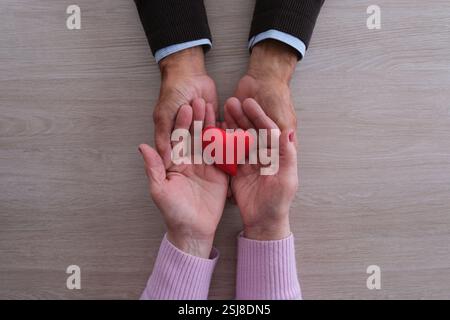 Elderly hands holding a red heart symbol in caring gesture Stock Photo