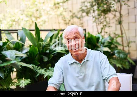 A cheerful senior man sitting outdoors in a lush garden, enjoying the sunshine. Stock Photo
