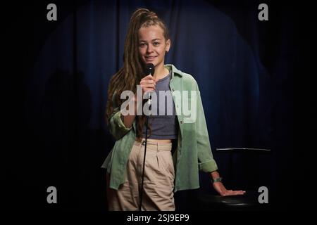 Portrait of smiling woman with long hair, holding microphone, standing on stage. Appearing confident and relaxed during stage performance Stock Photo