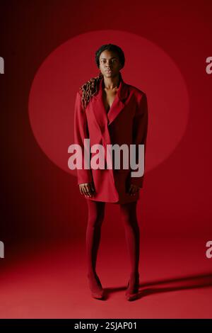 Portrait of African American woman standing against red background, wearing stylish red jacket and looking straight ahead, creating a striking, monochromatic effect Stock Photo