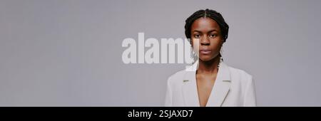 Portrait of black woman wearing white suit with serious expression and braids looking at camera against plain backdrop creating a professional and confident appearance Stock Photo