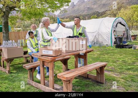 Two volunteers doing high five over donation boxes at table outdoors Stock Photo