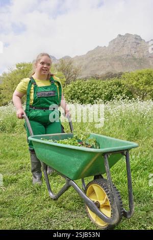 Female farmer walking with a wheelbarrow full of soil and looking at ...