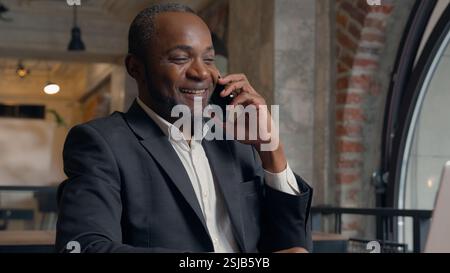 Happy smiling laughing African American positive ethnic man business employer entrepreneur smile pleasant conversation smartphone call talk mobile Stock Photo