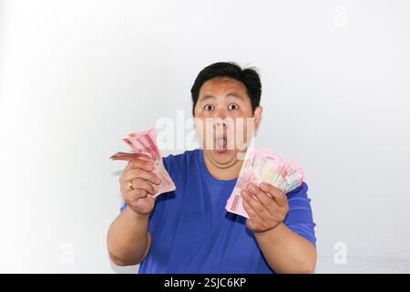 Surprised Man wearing blue tshirt Holding money Indonesian Rupiah from Bank Indonesian against isolated white background Stock Photo