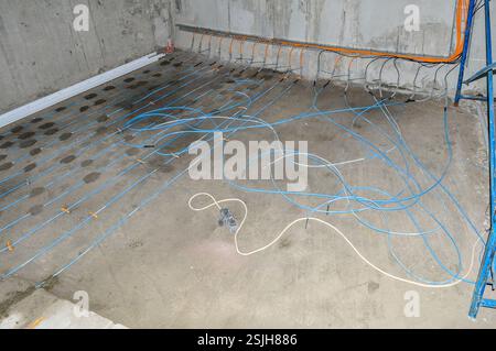 Installation of underfloor heating with blue pipes fixed with orange fasteners in a concrete room, ready for screed pouring. Stock Photo