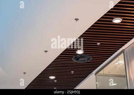 A modern ceiling design with alternating white panels and dark wood slats features recessed lighting and ventilation, creating a sleek aesthetic. Stock Photo