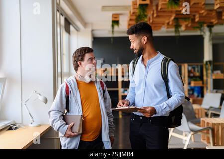 Young man with Down syndrome and his teacher talking while walking down the school hallway. Stock Photo