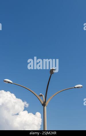 Outdoor scene showcasing a modern street lamp standing tall below a clear blue sky with clouds. Stock Photo