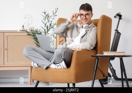 Young man with laptop sitting in armchair at home Stock Photo