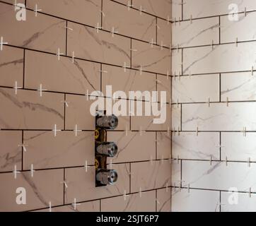 Shower wall under construction with white marble tiles and plastic spacers in home renovation project Stock Photo