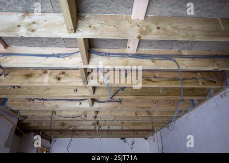 View of an unfinished ceiling featuring exposed wooden beams and electrical wires in a construction site interior Stock Photo