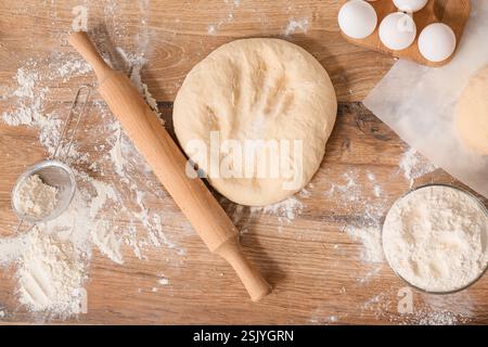 Fresh dough with rolling pin, flour and eggs on wooden table Stock Photo