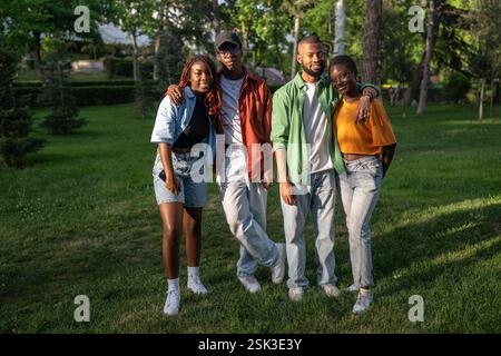 Joyful young black friends enjoying adventure in nature, standing by green park trees together Stock Photo