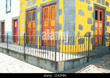 Building corner with a bright yellow facade, featuring large gray stones embedded in its walls. There are three wooden door and window framed by gray Stock Photo