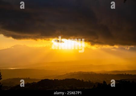 Golden Sunset Over Rolling Hills with Dramatic Dark Clouds and Sun Rays Breaking Through the Sky Stock Photo