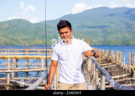 Young Filipino man in a white shirt shows off a freshly caught tilapia at a fish farm in Lake Buhi, Bicol, Philippines Stock Photo