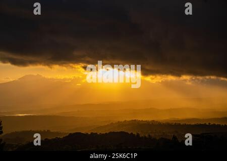 Golden Sunset Over Rolling Hills with Dramatic Dark Clouds and Sun Rays Breaking Through the Sky Stock Photo