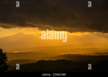 Golden Sunset Over Rolling Hills with Dramatic Dark Clouds and Sun Rays Breaking Through the Sky Stock Photo