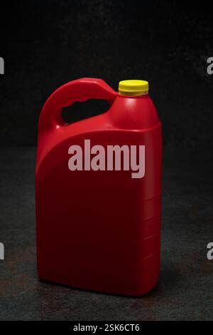Three-quarter view of red plastic motor oil bottle with handle and yellow screw-top without label on dark ceramic against black background Stock Photo