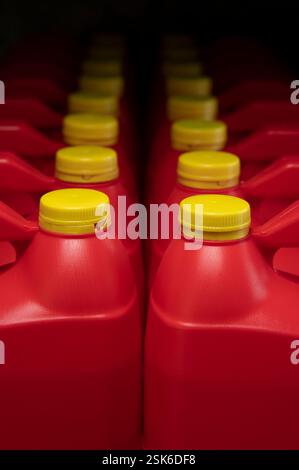 Front view of two columns of red plastic motor oil bottles, container with handle and yellow screw cap without label against dark background Stock Photo