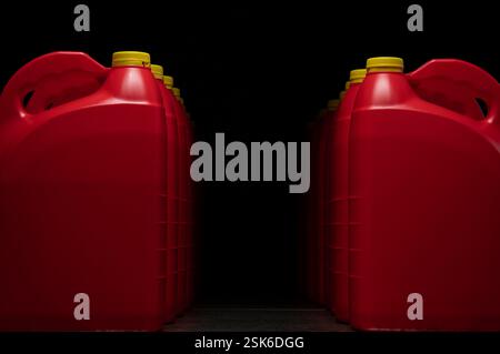 Front view of two columns of red plastic motor oil bottles forming a tunnel, containers with handle and yellow screw cap without label against dark ba Stock Photo