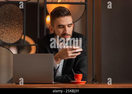 Portrait of young happy business man sitting at his desk in the office and using a phone. Stock Photo