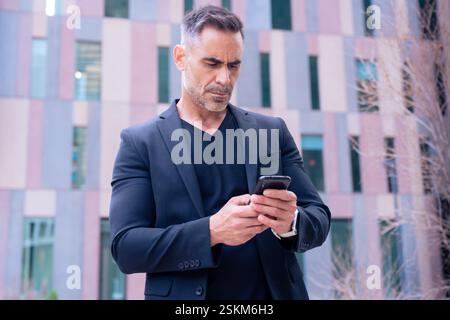 Confident businessman using smartphone outdoors, Stock Photo