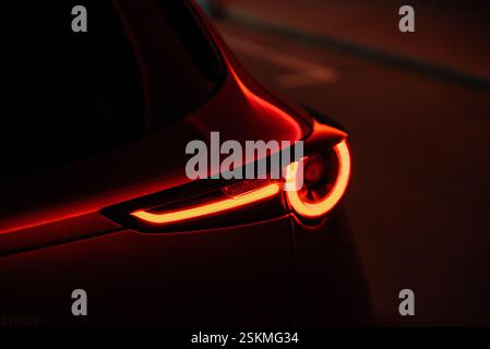 Tail light of modern red car at night. Close-up image of glowing LED tail lights in warm orange light. Reflection of street city lights on shiny metal Stock Photo