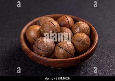 Shelled macadamia nuts sitting in small wooden bowl, creating appetizing arrangement on dark background Stock Photo