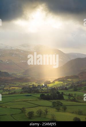 bright rays of sunshine breaking through dramatic clouds onto green fields in British Countryside. Lake District, UK. Stock Photo