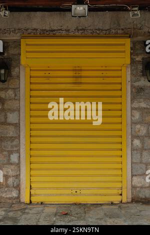 Slightly rusty yellow metal rolling door on a stone wall Stock Photo