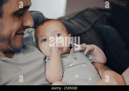Close-up of a smiling man sitting on a sofa with his baby son Stock Photo