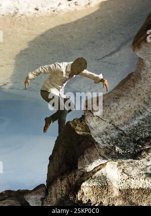 Upside down reflection in a lake of a dancer standing on a rock posing like a bird, Malta Stock Photo