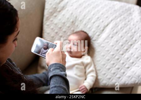 Woman Taking a Photo of her Newborn Baby son on a mobile phone Stock Photo