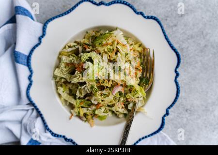 Overhead view of a bowl of cabbage, carrot and onion salad on a table with a tea towel Stock Photo