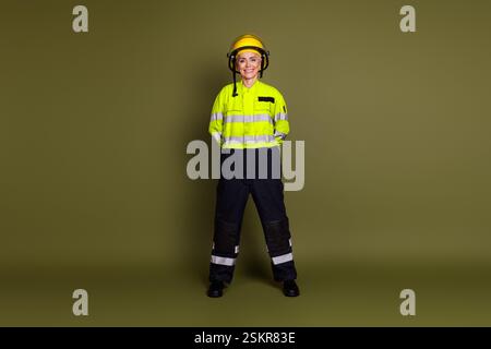 Smiling professional woman standing confidently in protective workwear against khaki background Stock Photo
